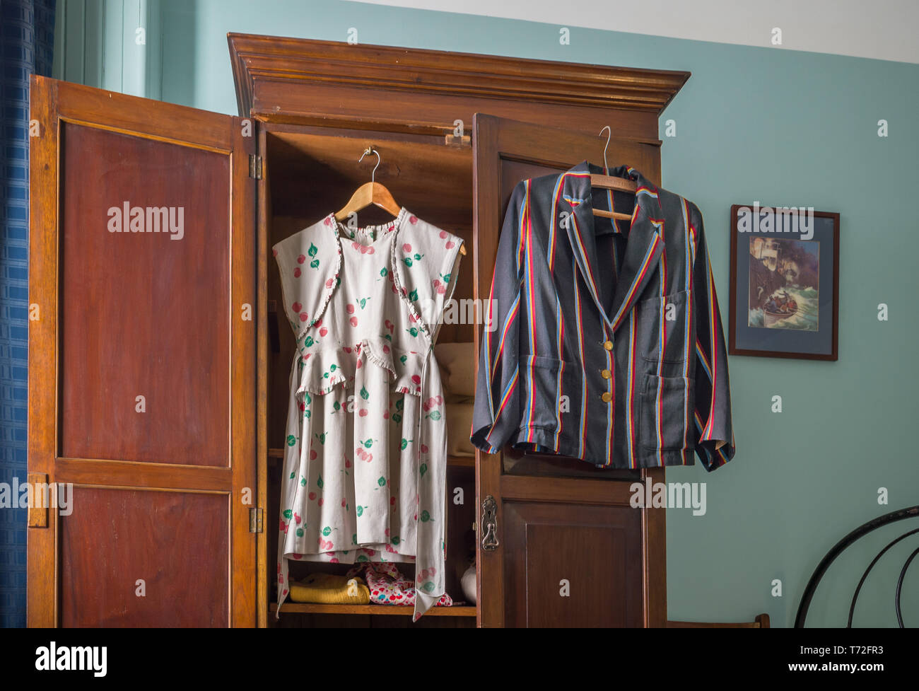 Typical bedroom from the 1940s and 1950s period with open wardrobe displaying a jacket and dress. Stock Photo
