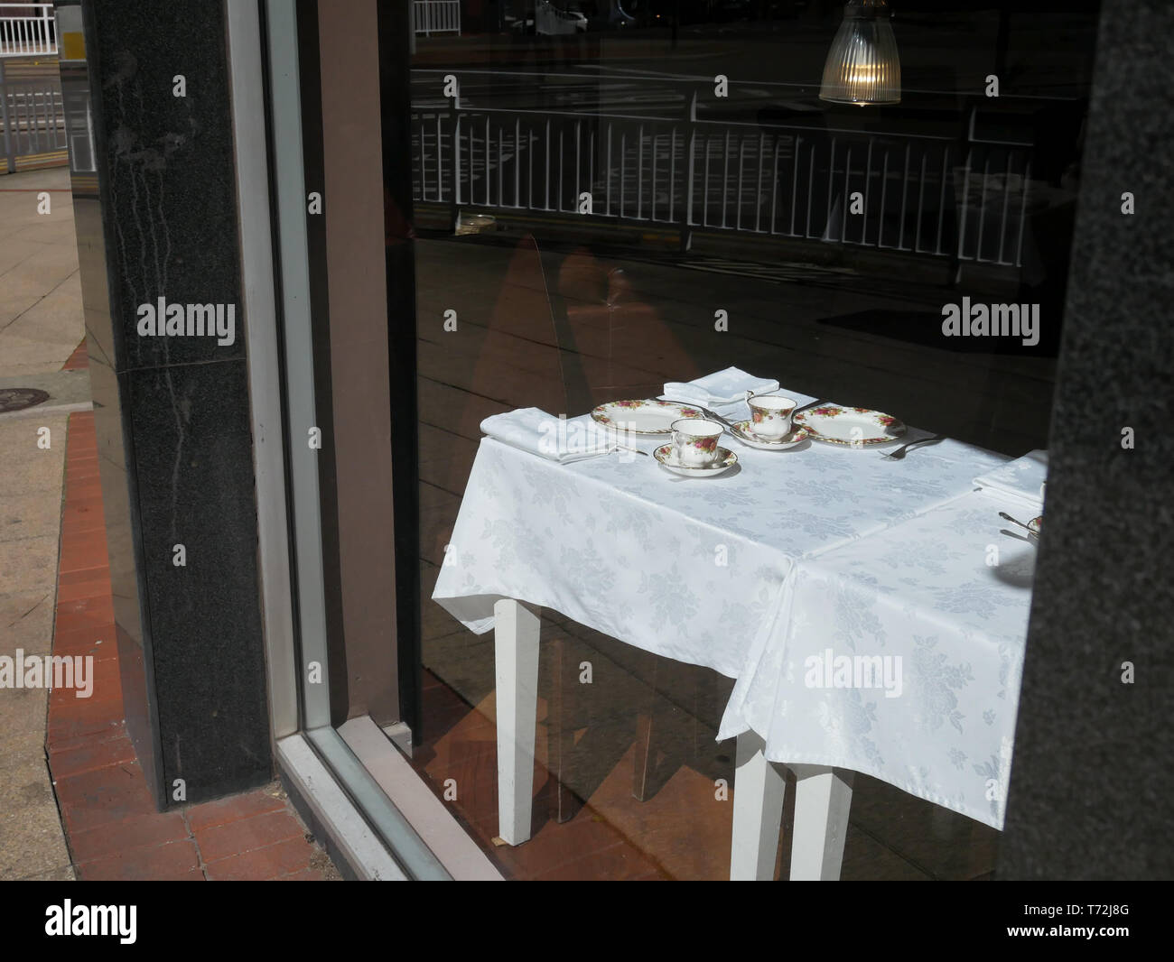 City corner cafe window with china tea service laid out and the street and railings reflected in the glass Stock Photo