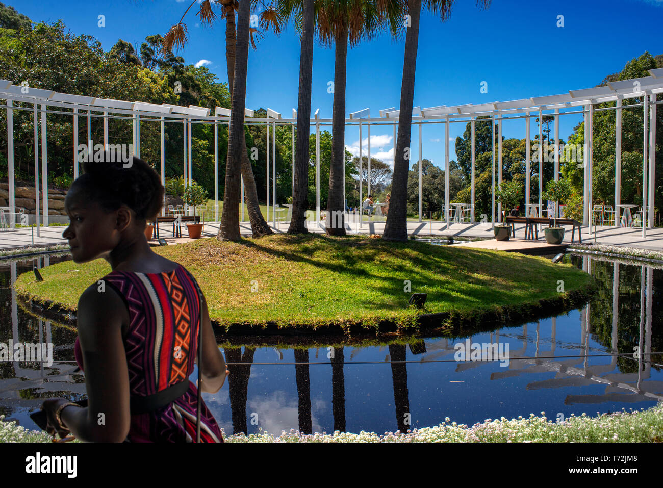 Black woman in The Calyx building at the Royal Botanic Gardens with people relaxing in the gardens in Sydney, Australia Stock Photo