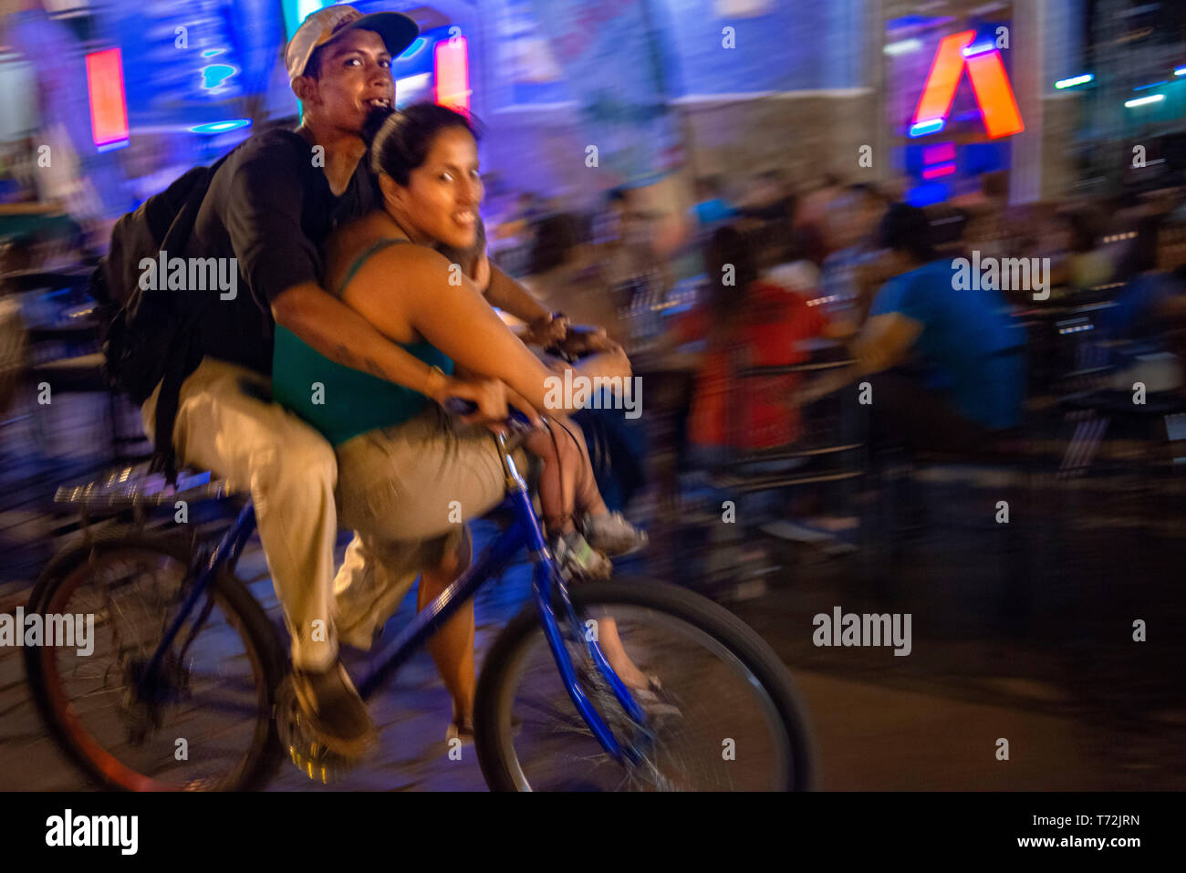 Local couple riding a bicycle in La Calzada a gastronomic street in Granada Nicaragua with lots of tourists and locals enjoying fine food outdoors. Gr Stock Photo
