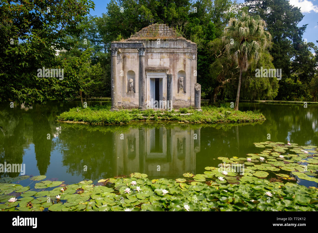The English garden of the 'Reggia di Caserta' has a few fake ruins, like this temple ruin on a small island in the middle of a pond with lilies. Stock Photo