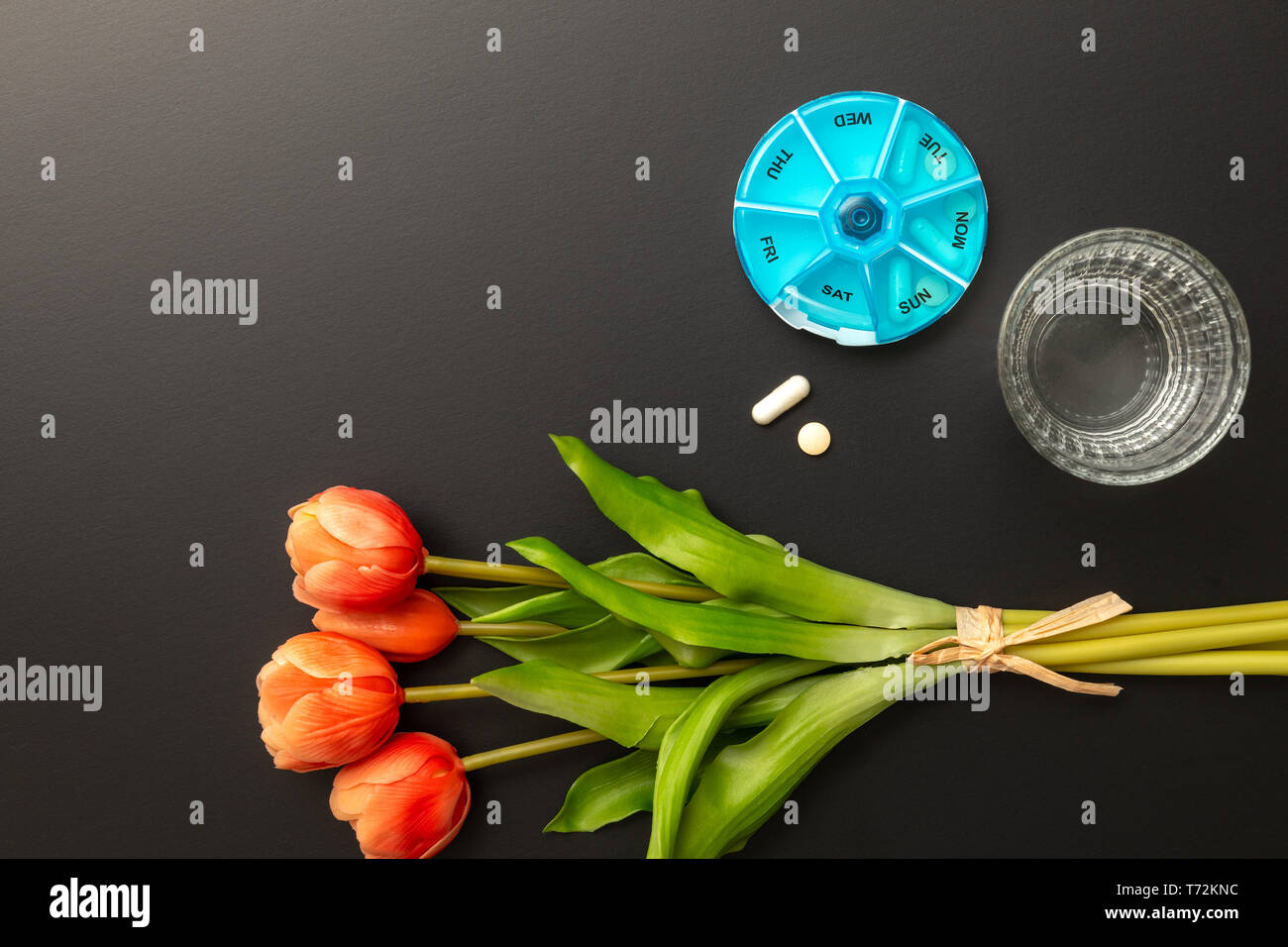 open pillbox with some pills glass of water and tulips Stock Photo