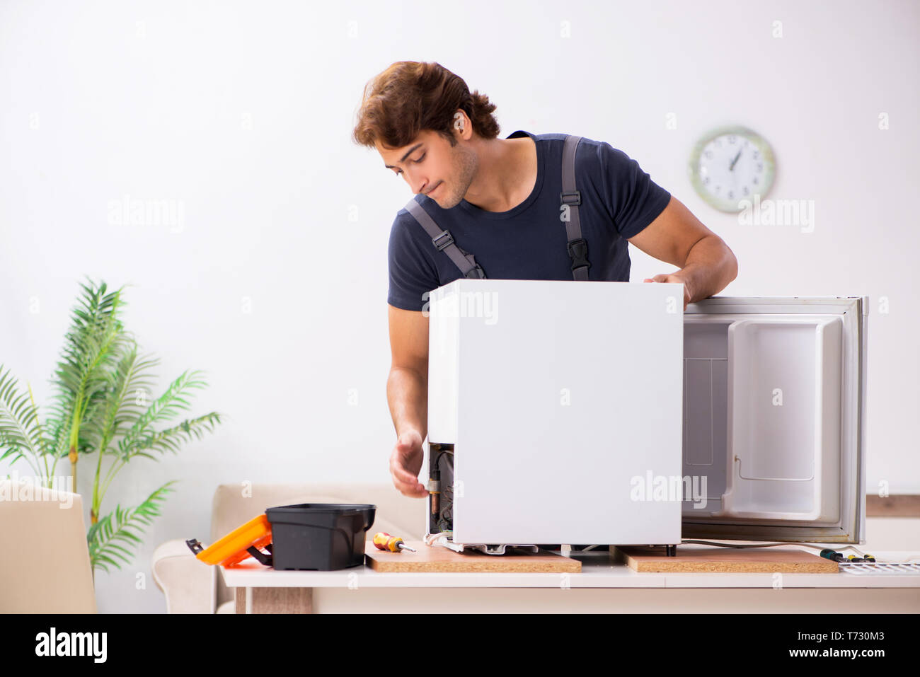 Young handsome contractor repairing fridge Stock Photo