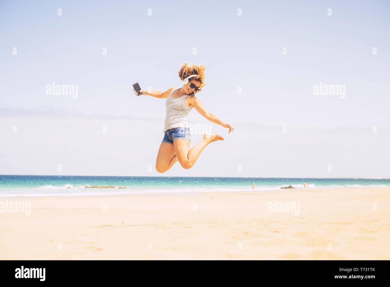 People happines concept for summer holiday vacation leisure activity at the beach - young crazy beautiful blonde woman jump with phone and headphones  Stock Photo