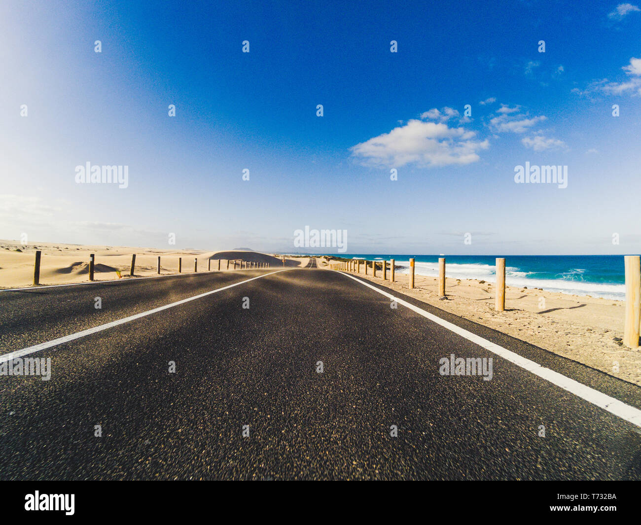 Long way road for travel car transportation concept with desert and beach on the side - sea water and blue clear beautiful sky in background - motion Stock Photo