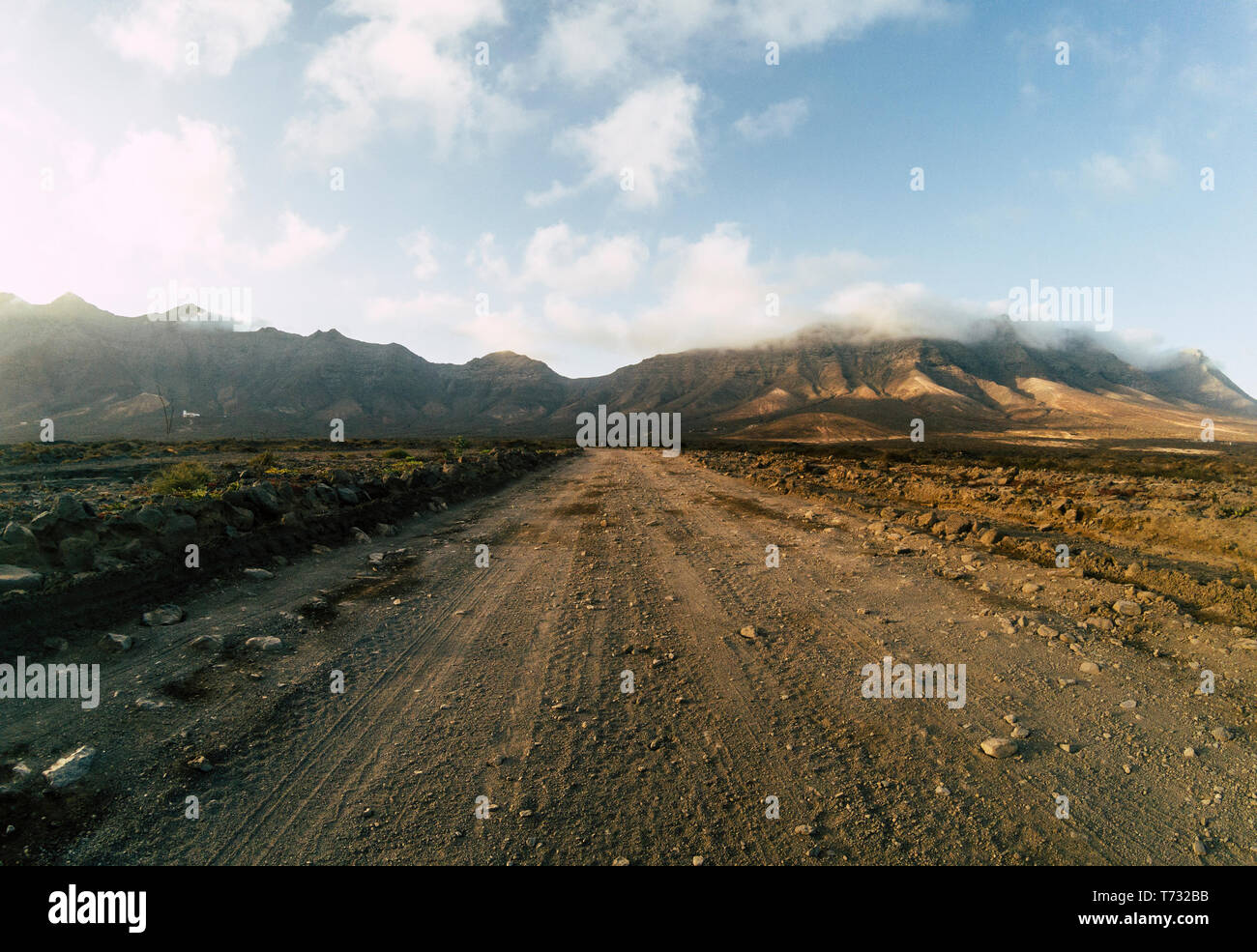 Long off road terrain way road viewed from ground level with mountains and blue cloudy sky - travel and adventure concept for alternative vacation and Stock Photo