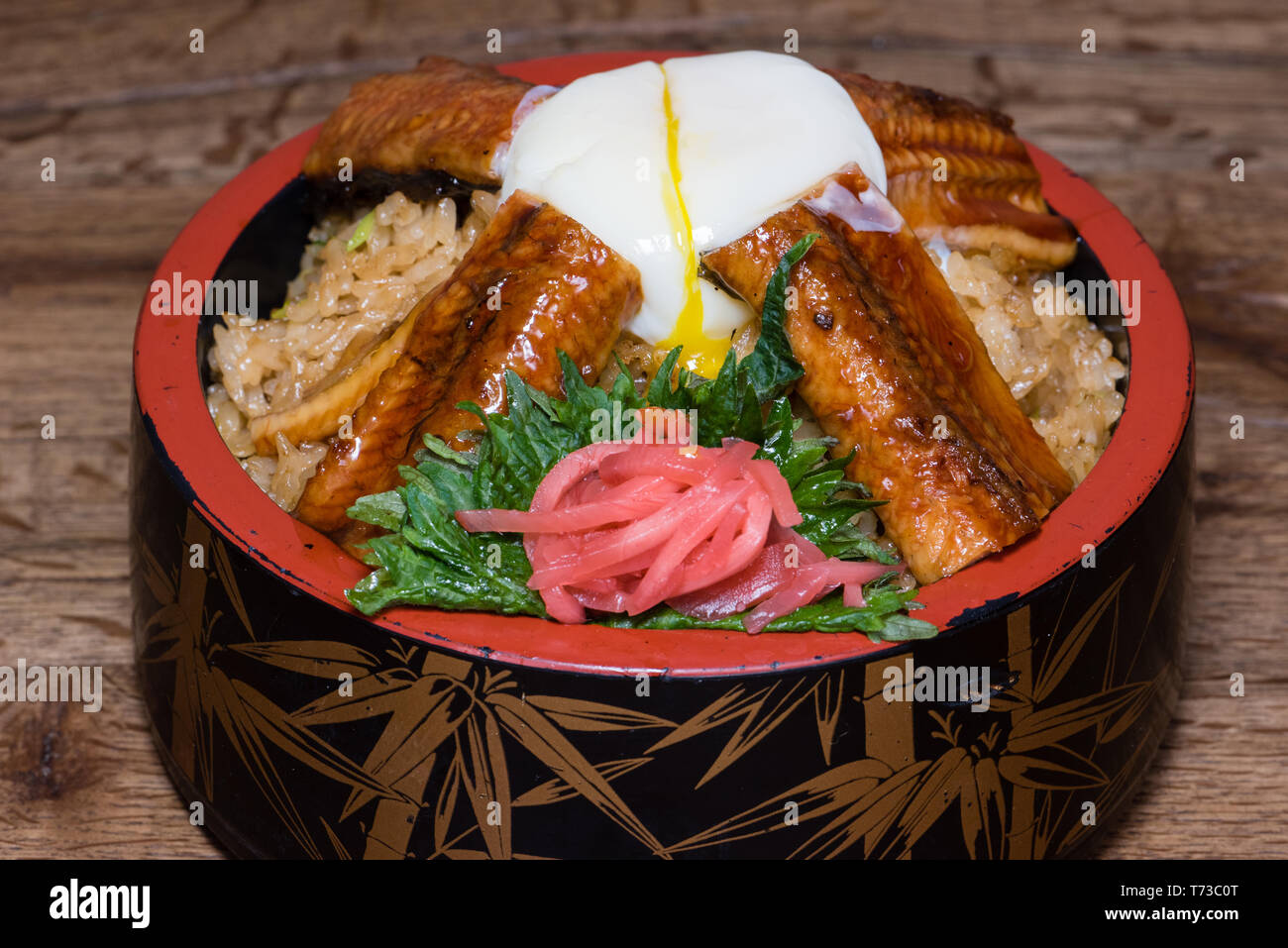 Japanese fusion dish with spicy rice with tamari sauce, roasted eel, egg and red turnip, in a decorated bowl, dark wood table background Stock Photo