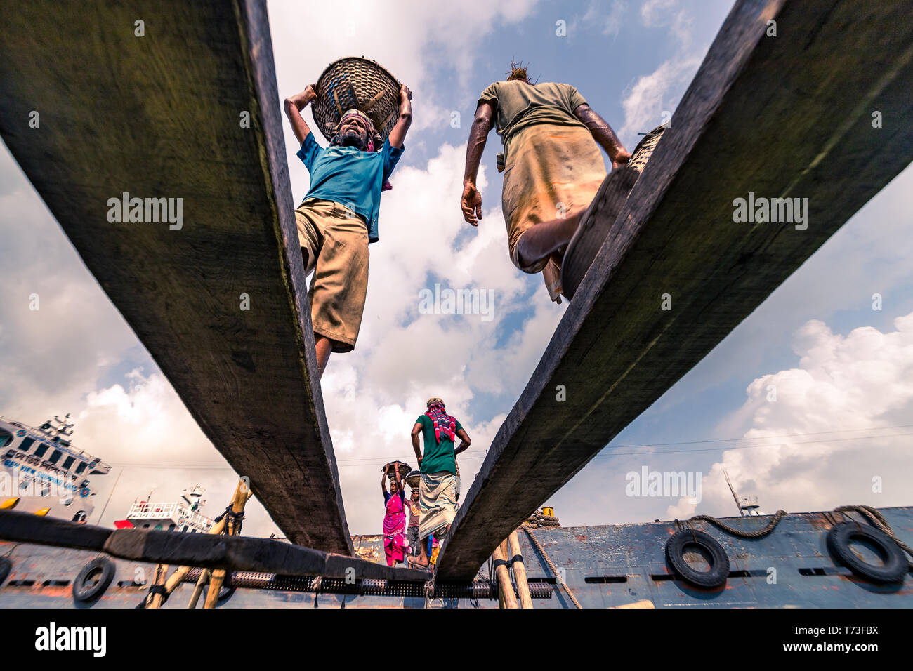 Male & Female dock workers are seen as they unload coal with bamboo baskets from ferries at Buriganga river port in Dhaka, Bangladesh. Stock Photo