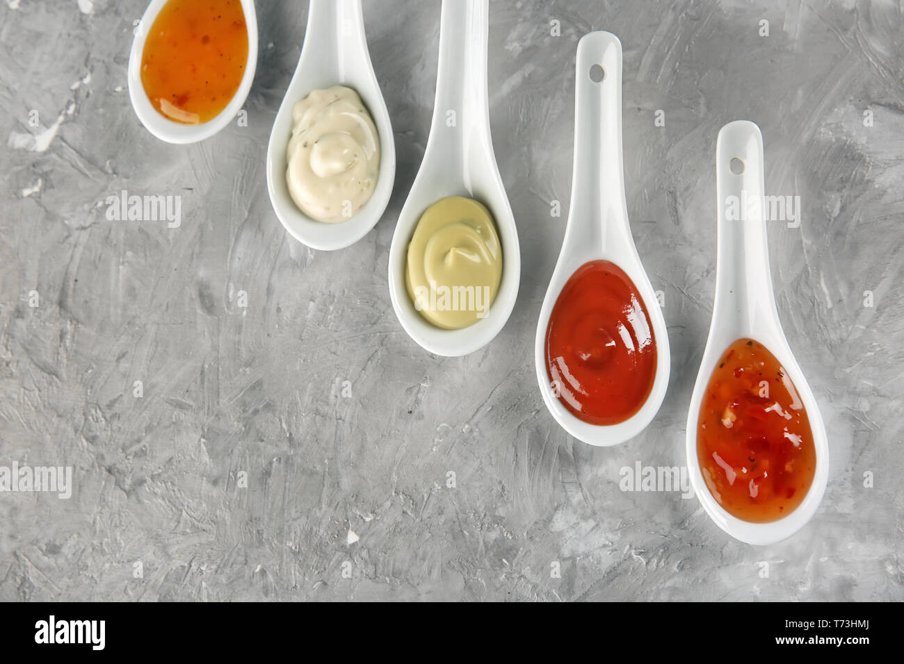 Ceramic spoons with different sauces on grey background, top view Stock Photo