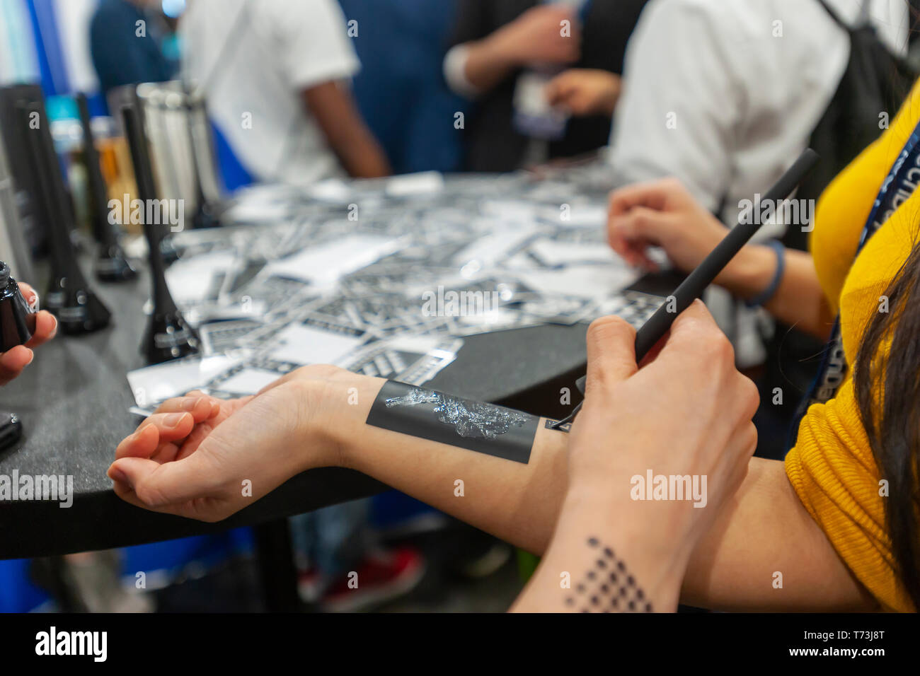 Representatives from Amkiri apply temporary tattoo stencils with fragrances at the TechDay New York event on Thursday, May 2, 2019. Thousands attended to seek jobs with the startups and to network with their peers, and perhaps to find the next big startup. TechDay bills itself as the U.S.'s largest startup event with over 350 exhibitors and over 20,000 attendees. (Â© Richard B. Levine) Stock Photo