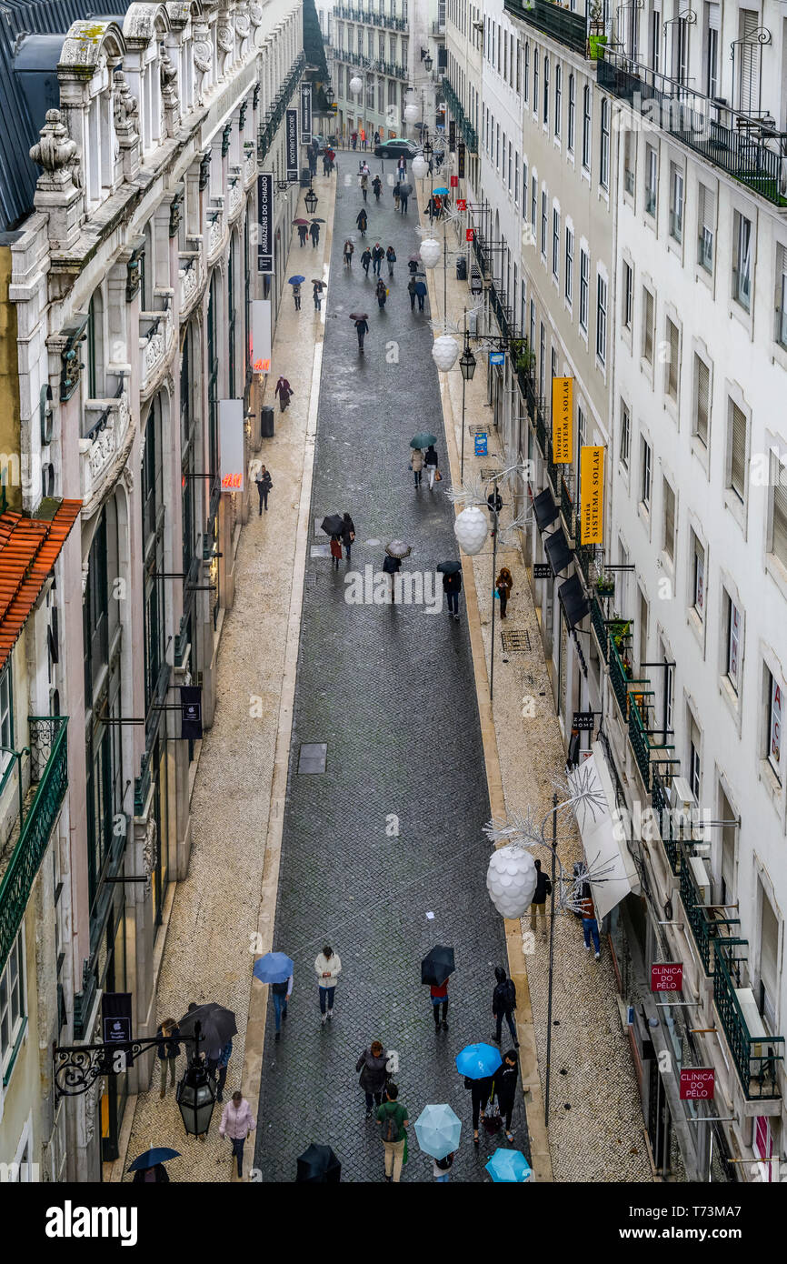 Pedestrians with umbrellas walk the narrow street in between buildings