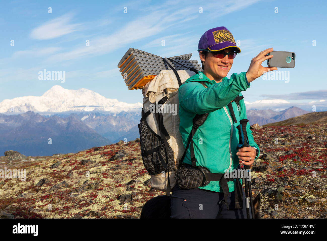 Woman taking selfie while backpacking with Denali in the background, along the Kesugi Ridge Trail, Denali State Park on a sunny autumn day, Southce... Stock Photo