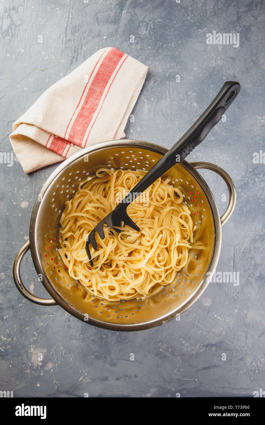 Italian pasta linguine in a metal colander on grey background. Top view