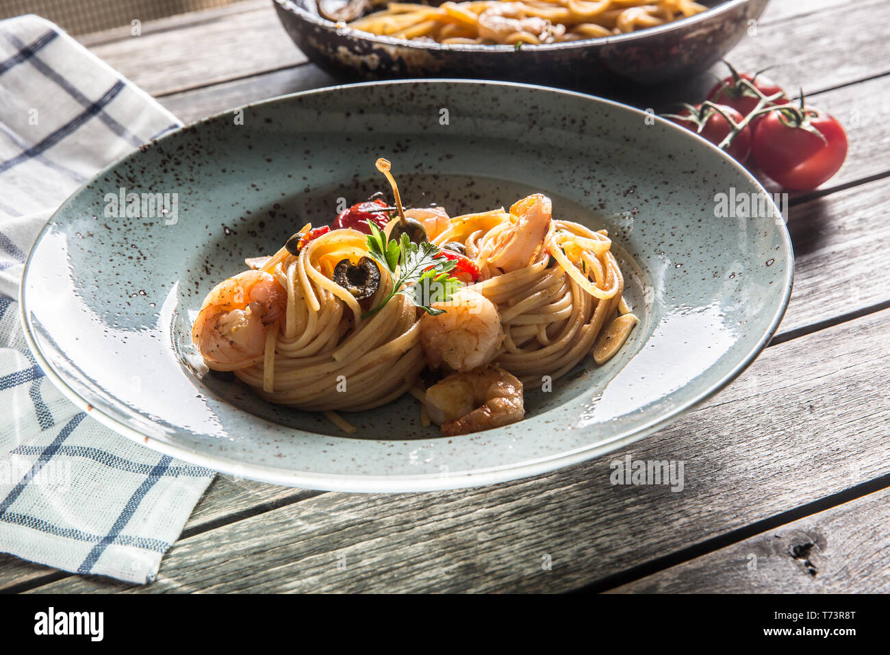 Pasta spaghetti on plate and pan with shrimp tomato sauce toatoes and herbs. Italian or mediterranean cuisine. Stock Photo