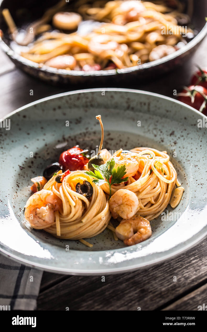 Pasta spaghetti on plate and pan with shrimp tomato sauce toatoes and herbs. Italian or mediterranean cuisine. Stock Photo