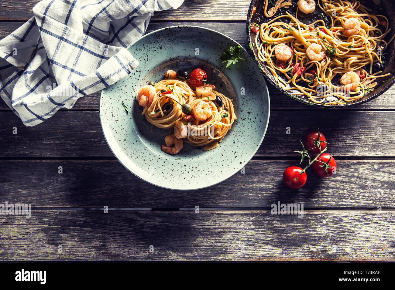 Pasta spaghetti on plate and pan with shrimp tomato sauce toatoes and herbs. Italian or mediterranean cuisine. Stock Photo