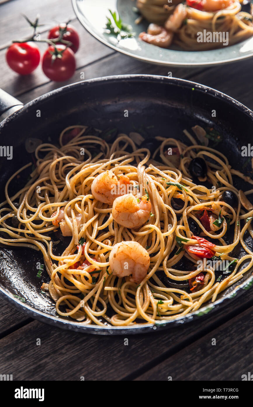 Pasta spaghetti on plate and pan with shrimp tomato sauce toatoes and herbs. Italian or mediterranean cuisine. Stock Photo