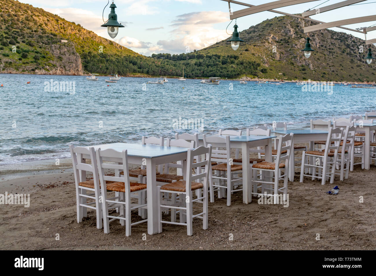 Traditional greek tavern with wooden tables on sandy beach near water waiting for tourists in Tolo, Peloponnese, Greece, vacation season is starting Stock Photo
