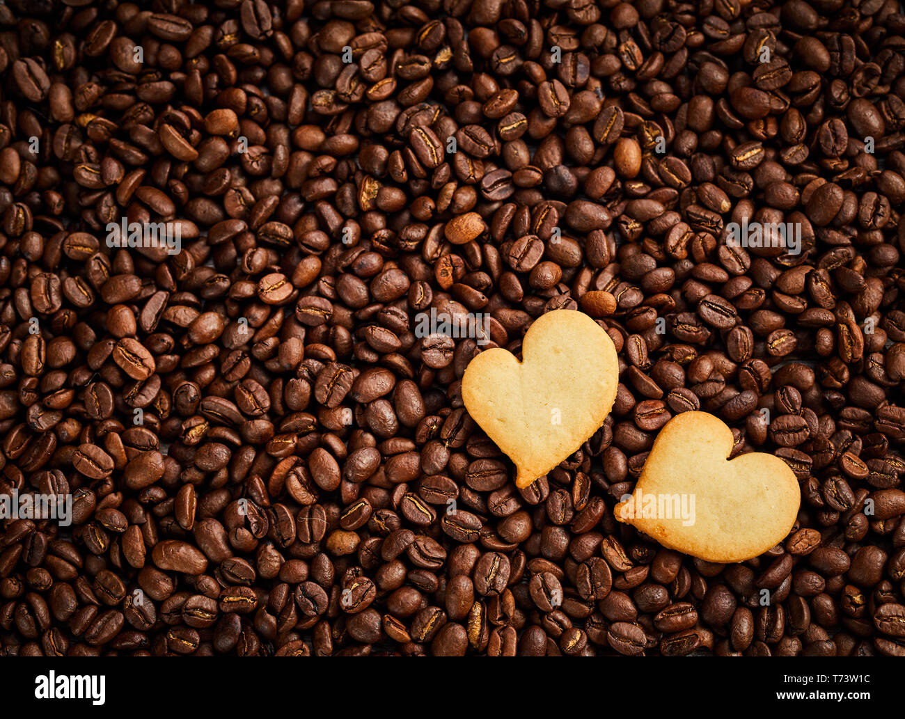 Roasted coffee bean background with fresh pastries or heart-shaped biscuits in the corner conceptual of love, like, friendship or Valentines Day Stock Photo