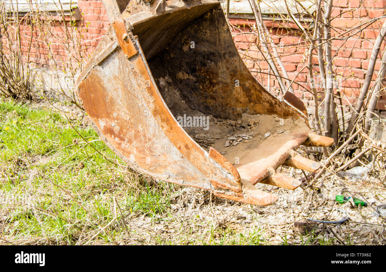 Old, rusty and dirty excavator bucket closeup on brick wall background. Stock Photo