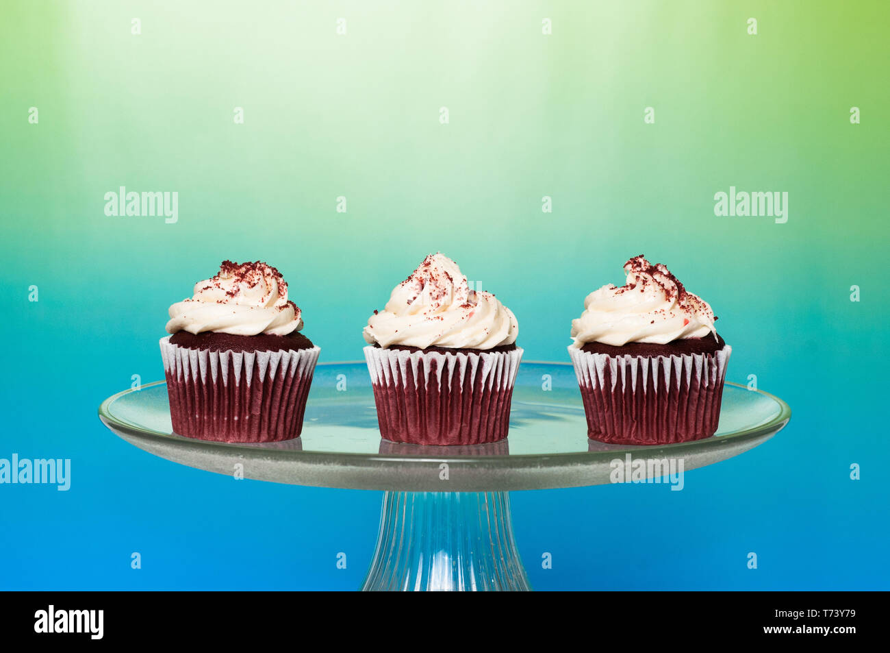 three frosted cupcakes on a cake stand with a bright colorful background Stock Photo