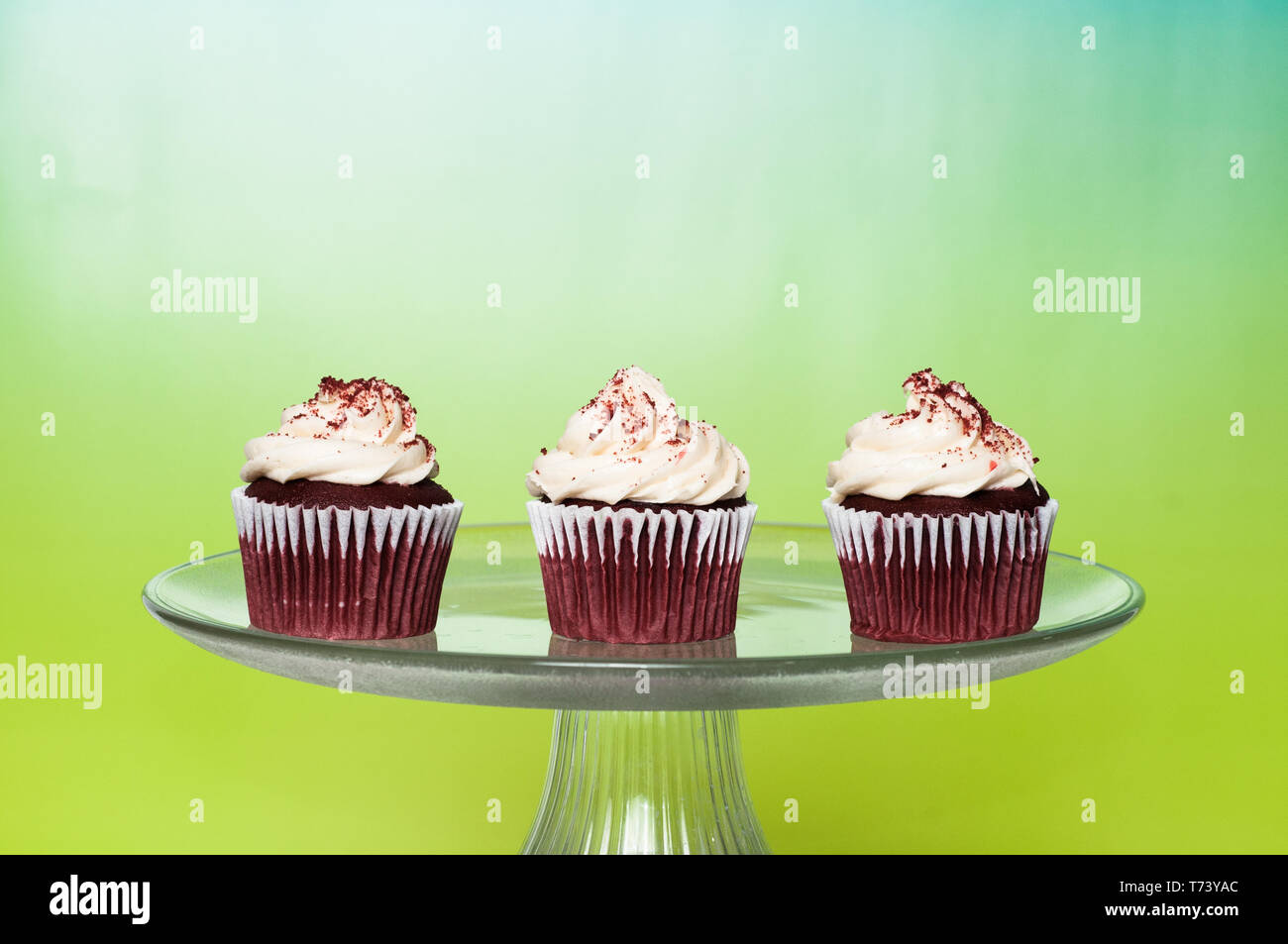 three frosted cupcakes on a cake stand with a bright colorful background Stock Photo