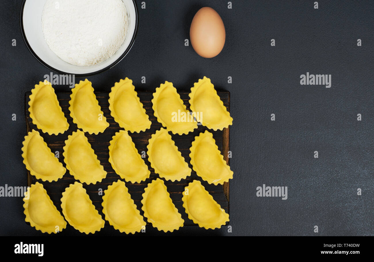 Creative layout made of uncooked ravioli pasta,flour in the bowl and one egg . Horizontal orientation with copy space. Food concept. Stock Photo