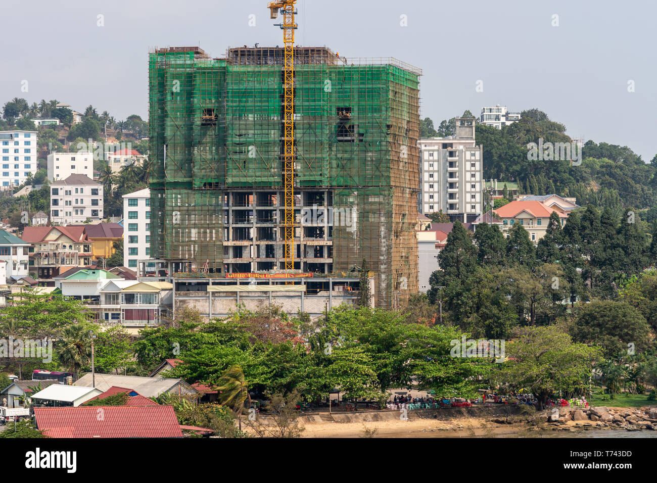 Sihanoukville, Cambodia - March 15, 2019: Large highrise construction site wrapped in green with yellow crane in Sihanouk Autonomous Port neighborhood Stock Photo