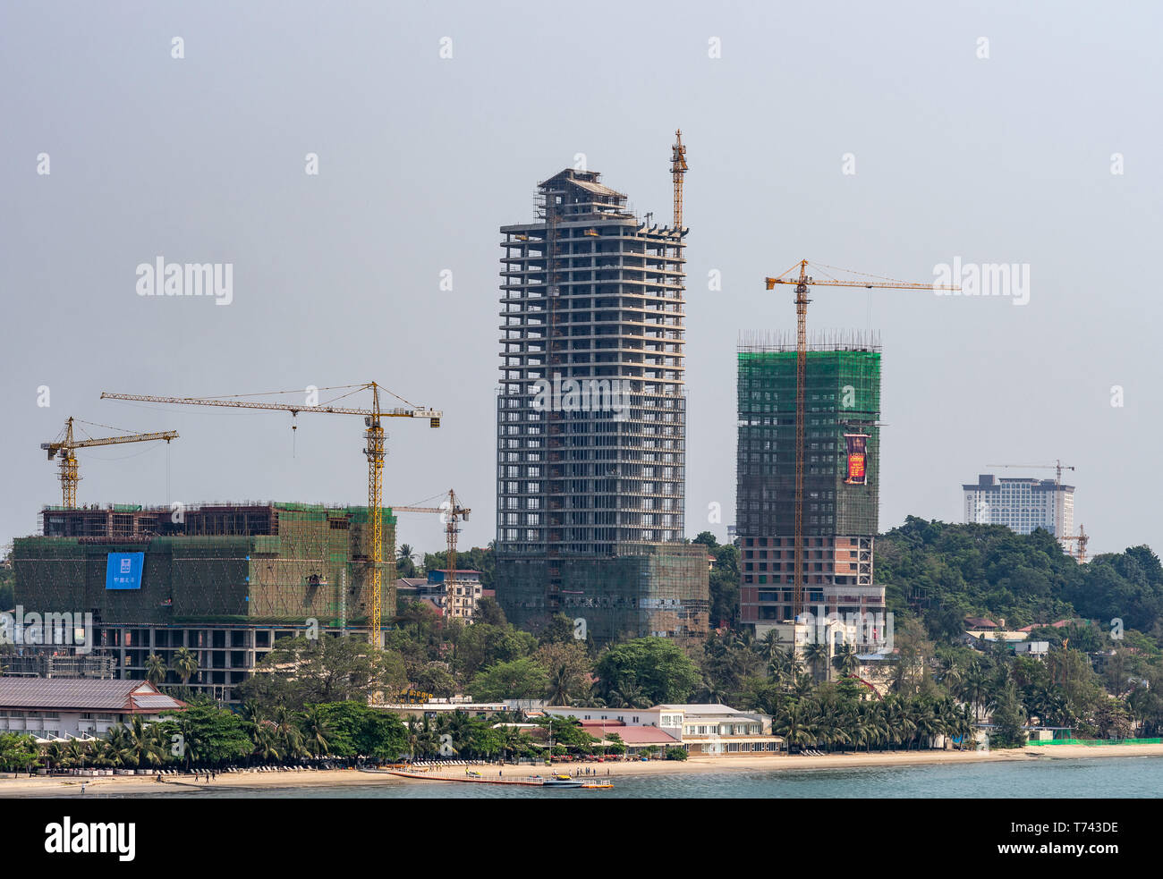Sihanoukville, Cambodia - March 15, 2019: Shoreline turned into massive construction site of tall high rise buildings under light blue sky, yellow cra Stock Photo