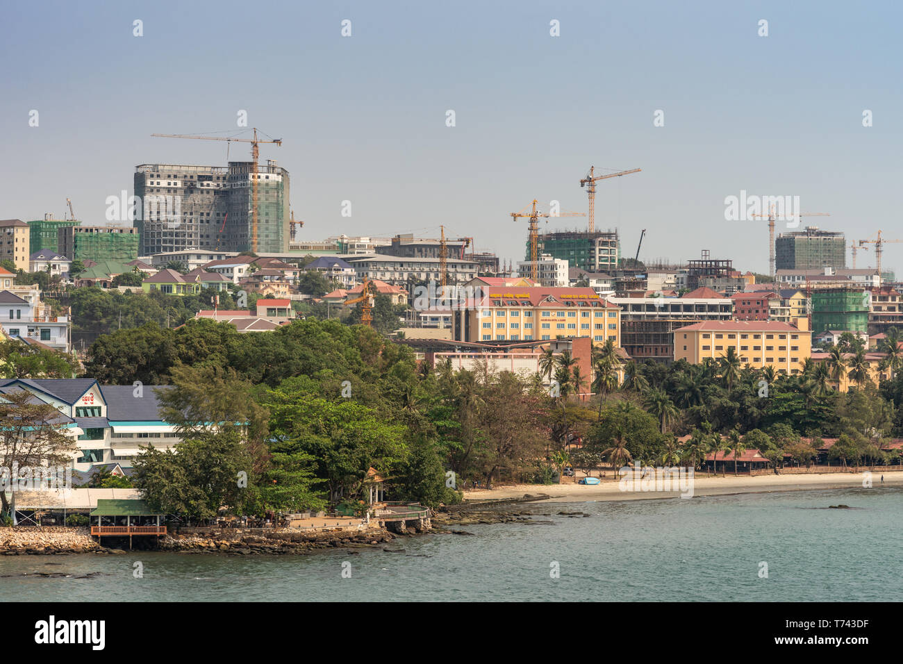 Sihanoukville, Cambodia - March 15, 2019: Town turned into massive construction site of tall high rise buildings under light blue sky, yellow cranes.  Stock Photo