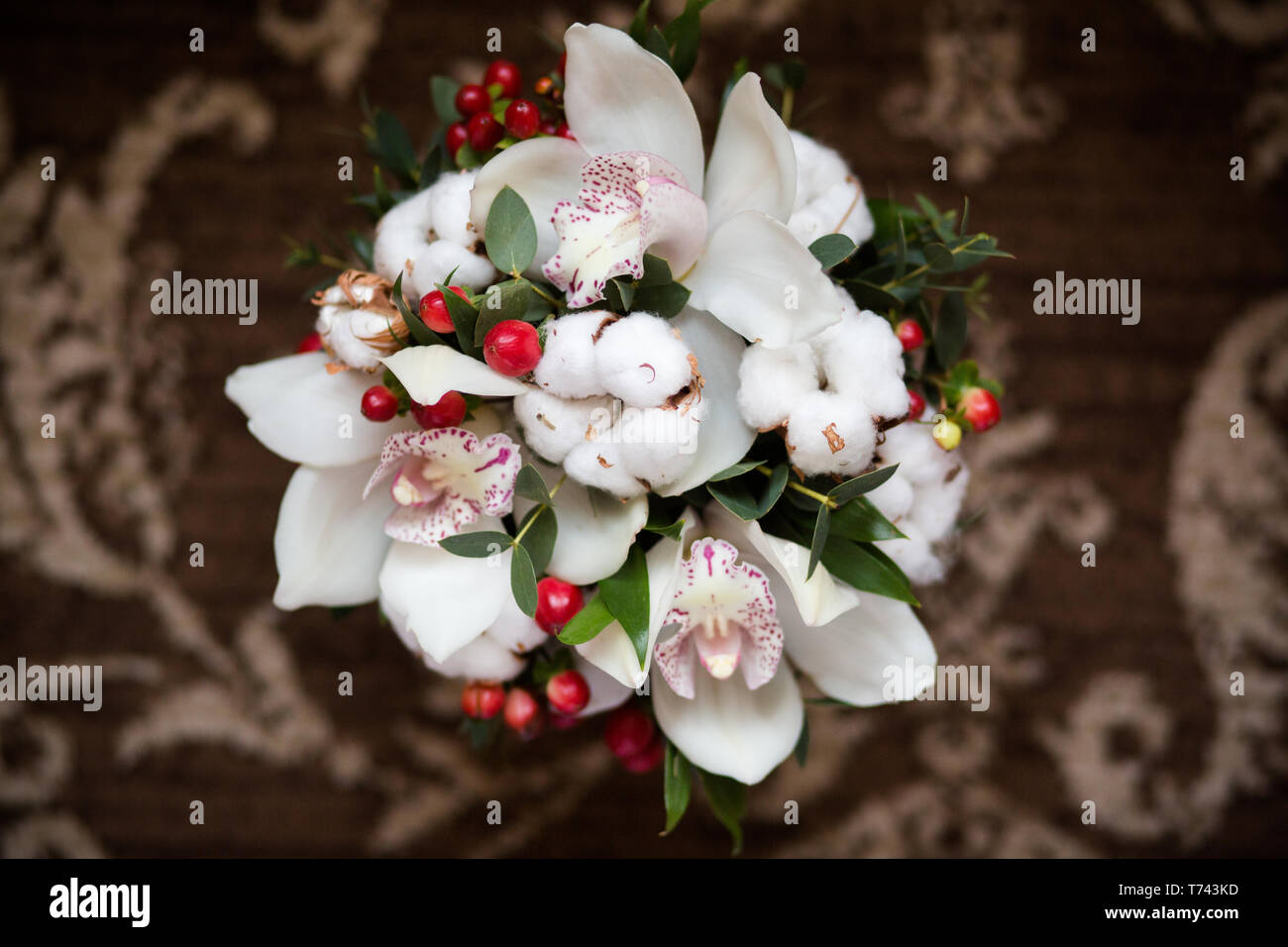 A miniature bouquet of orchids and a branch of blossoming cotton, complemented by red hypericum berries Stock Photo