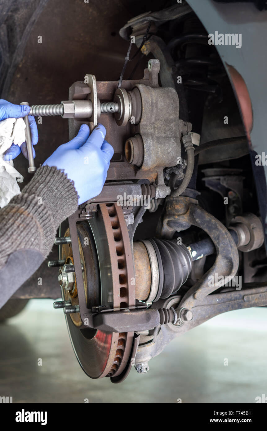Mechanic changing the brake pads of a car and pressing the plunger of