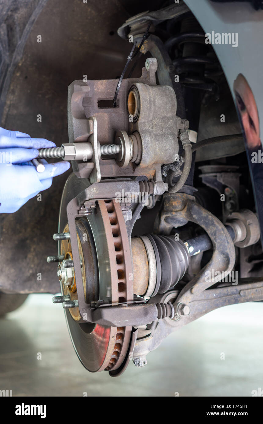 Mechanic changing the brake pads of a car and pressing the plunger of