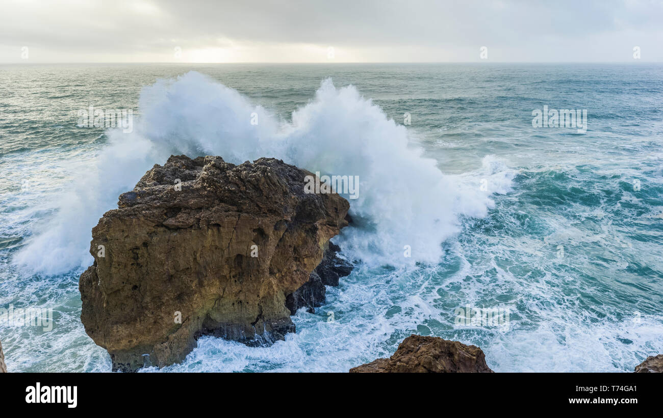 sea with big waves crashing to shore and rocks