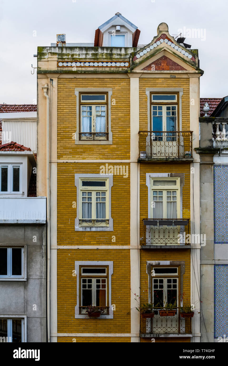 Facade of a tall, yellow brick residential building with small balconies and windows; Lisbon, Lisboa Region, Portugal Stock Photo