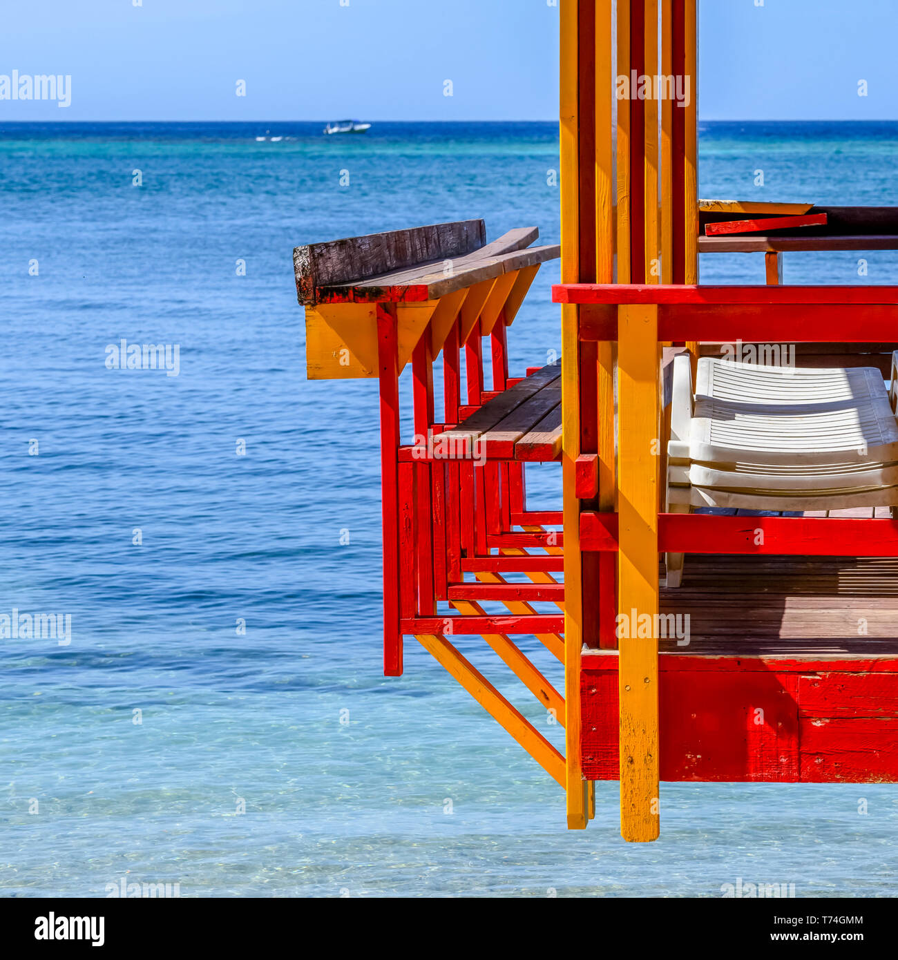 Colourful painted dock with lounge chairs and the Caribbean Sea with a boat in the distance; Roatan, Bay Islands Department, Honduras Stock Photo