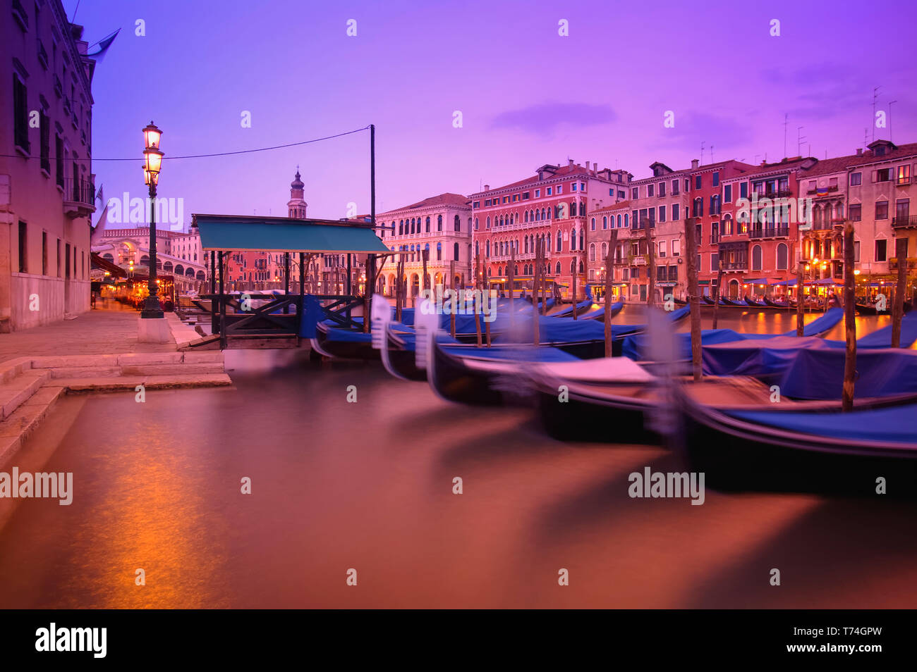Gondolas moored along the shoreline of the Grand Canal during a vibrant sunset; Venice, Italy Stock Photo