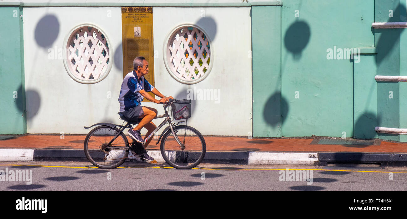 A Chinese man cycling a bike bicycle past Chulia mosque on South Bridge Road Chinatown Singapore. Stock Photo