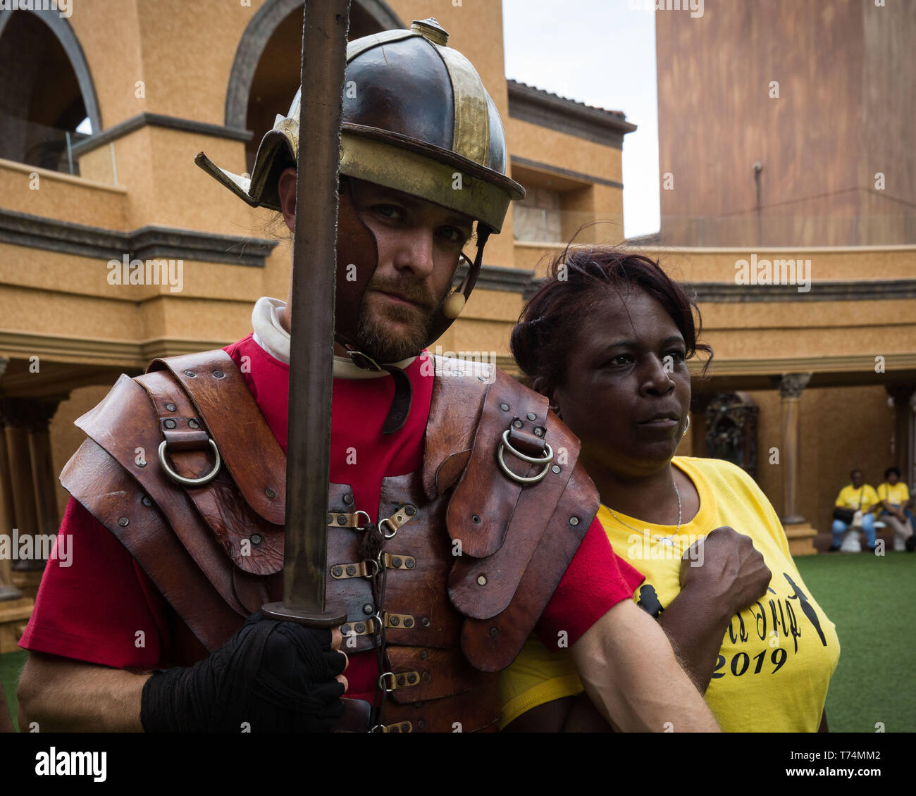 May 3, 2019 - Orlando, Florida, U.S - A woman visiting from South Carolina poses for a photo with an actor after participating in a Roman soldier training camp at The Holy Land Experience (HLE) in Orlando, Florida. The theme park, owned by the Trinity Broadcasting Network, recreates the architecture and themes of the ancient city of Jerusalem in 1st-century Judea. HLE is a non-denominational Christian living biblical museum and church. There are multiple religious-themed live performances given throughout the day in various locations, inside and out. (Credit Image: © Tracy Barbutes/ZUMA Wire) Stock Photo