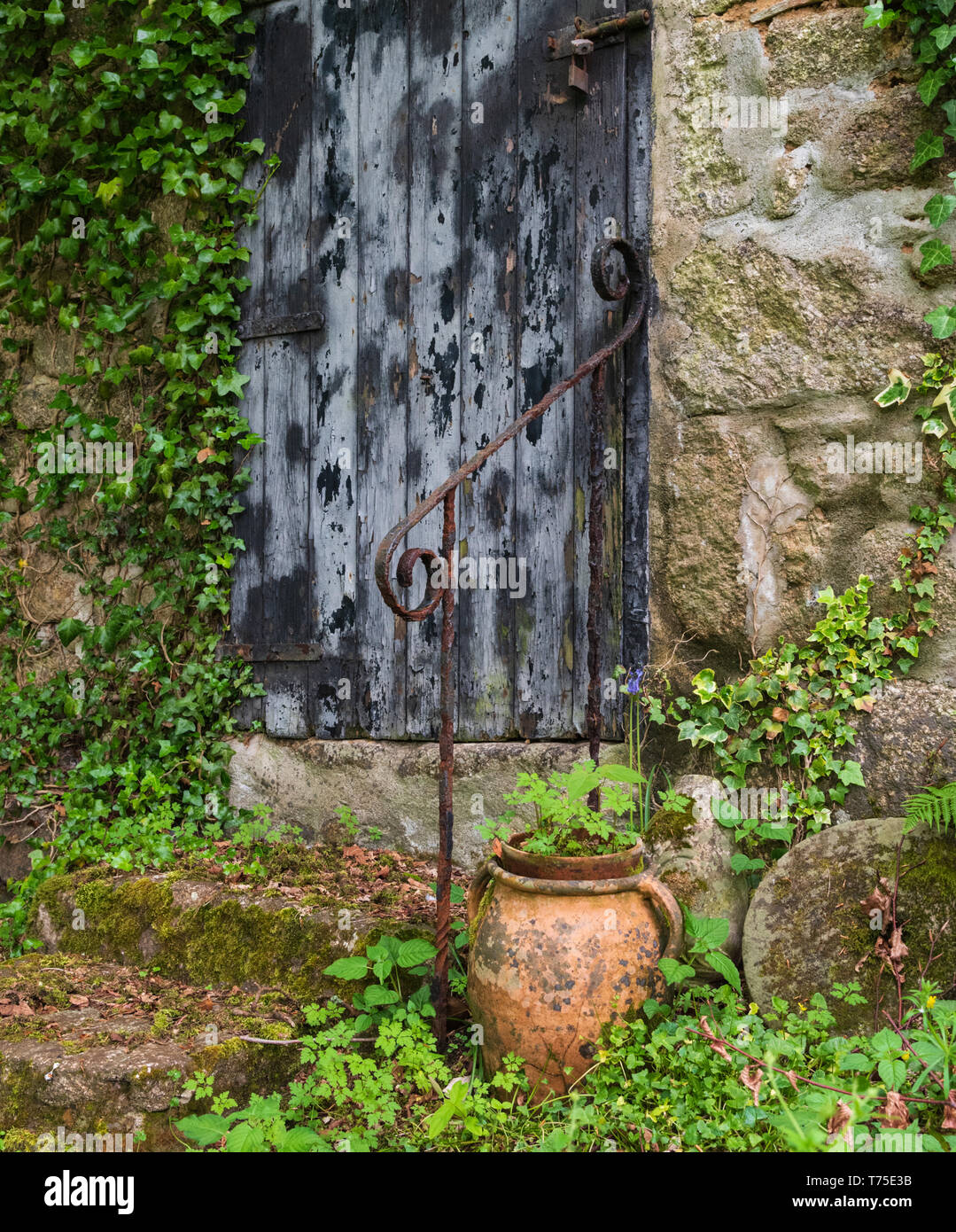 Old doorway and steps to disused watermill with cast iron handrail, old millstones and a terracotta pot in Lamorna, Cornwall, UK. Stock Photo