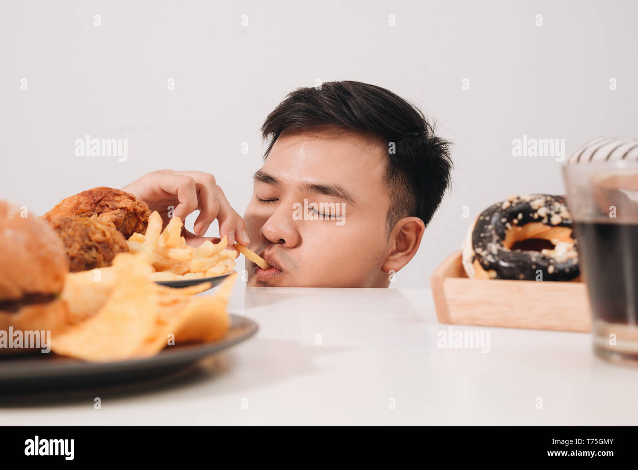 Young man having cravings for donuts, hamburger, chicken with fries instead Stock Photo