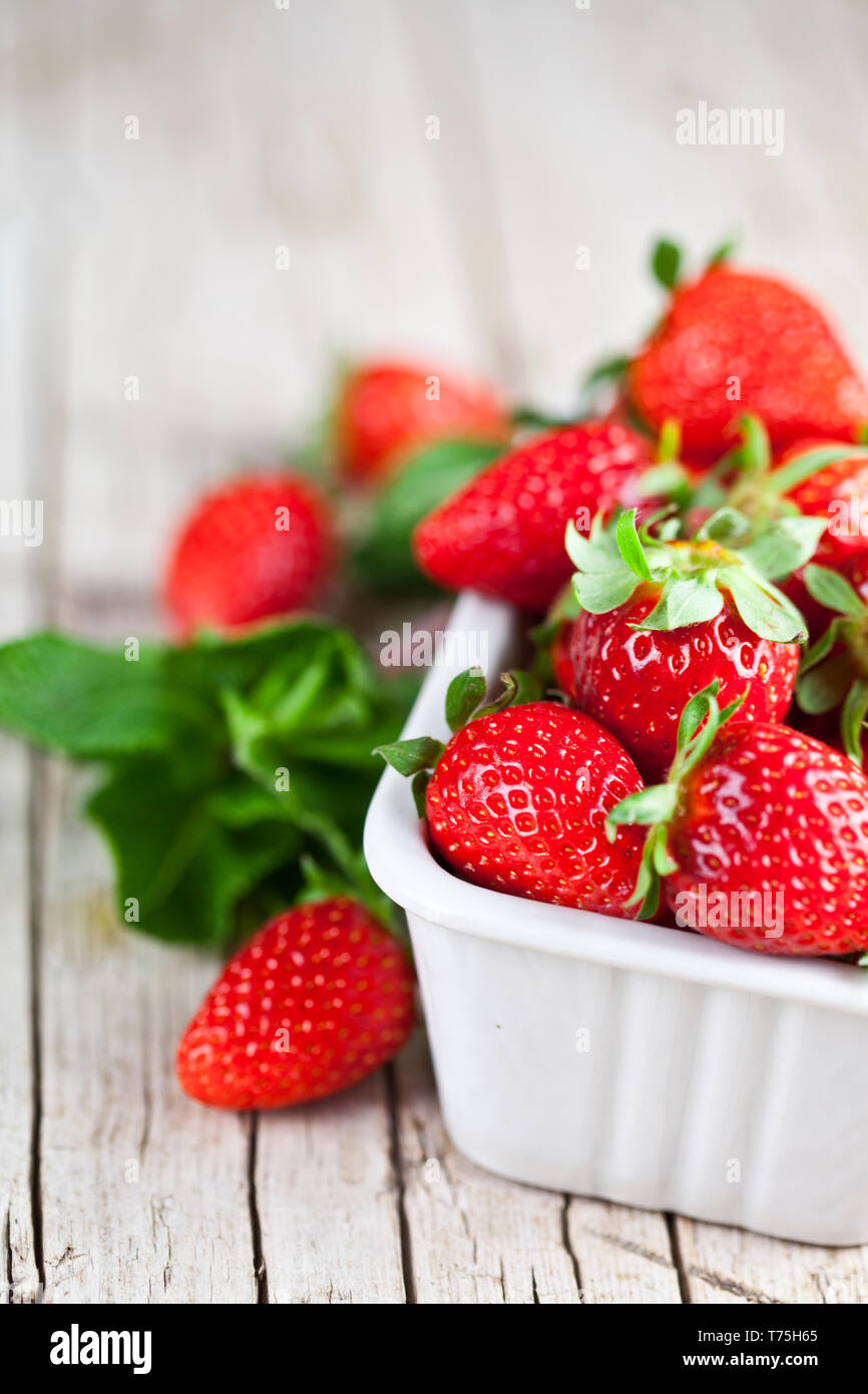 Fresh red strawberries in white bowl and mint leaves on rustic wooden ...