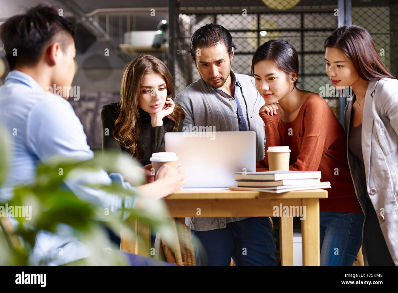 group of young entrepreneurs asian and caucasian man and woman meeting in office discussing business using laptop computer. Stock Photo