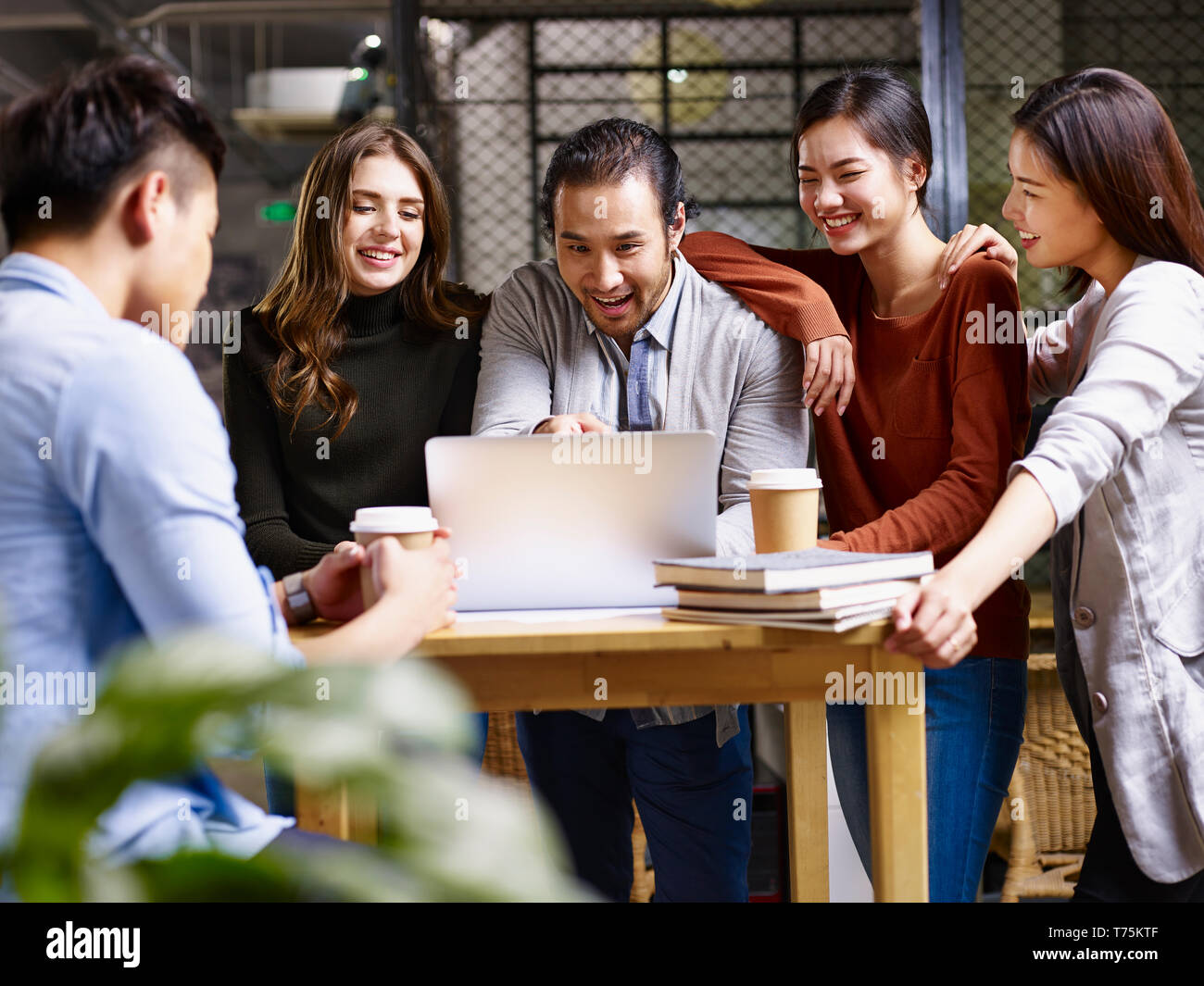group of happy young entrepreneurs asian and caucasian man and woman meeting in office discussing business using laptop computer. Stock Photo