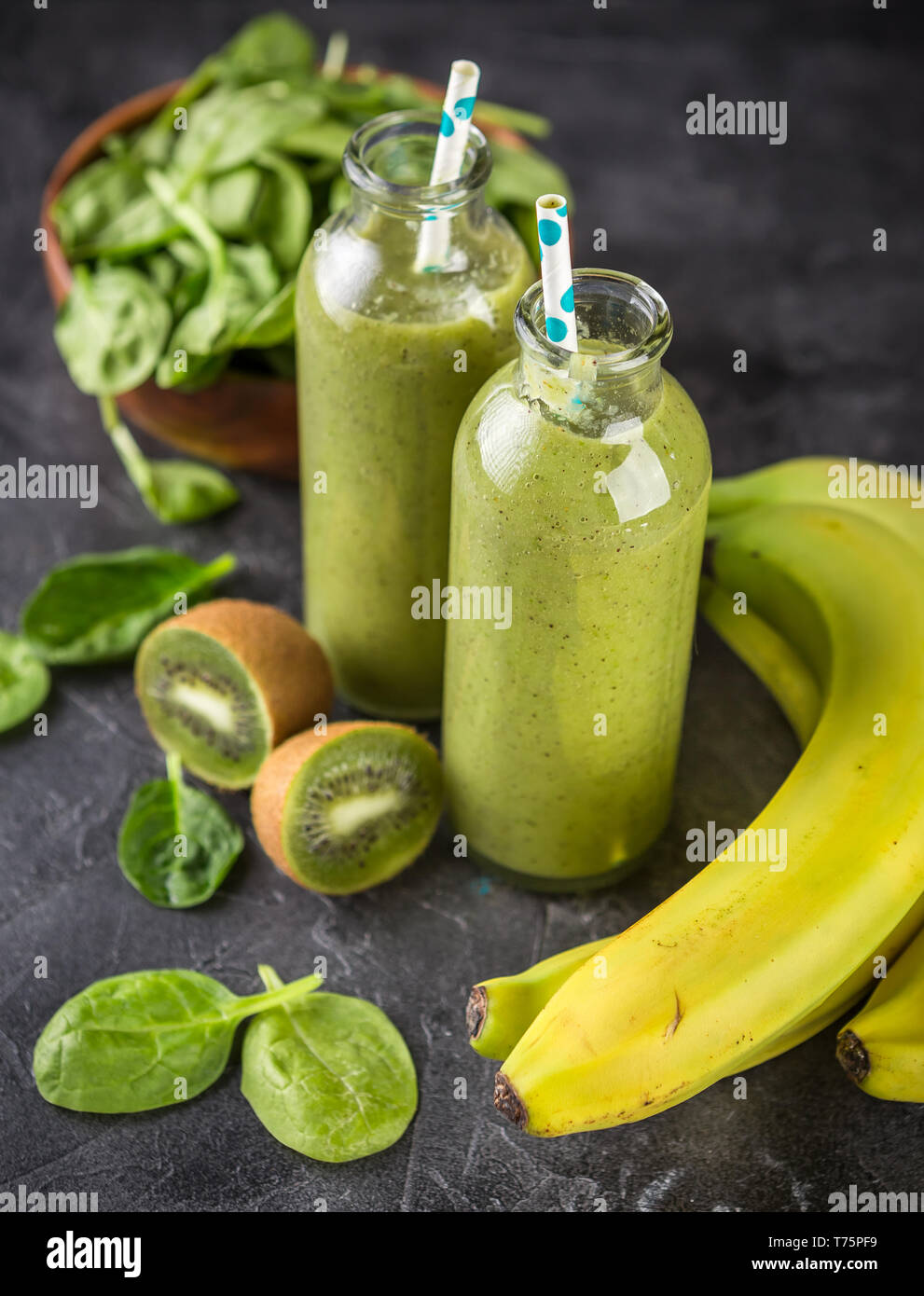 Healthy green smoothie in glass bottles and spinach, bananas, kiwi on a