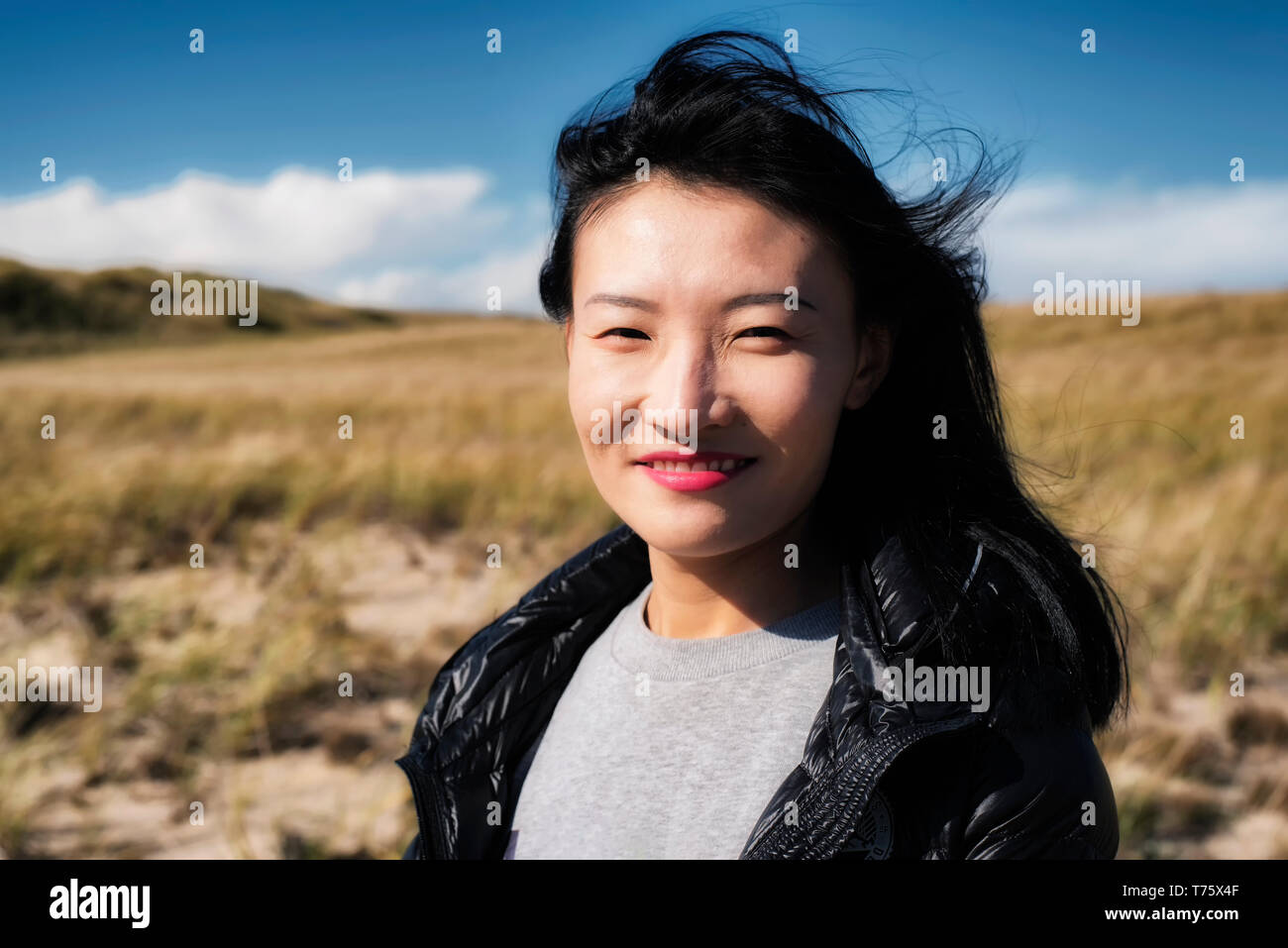 A chinese woman smiling outside on a sunny windy day on the cape cod national seashore in Truro Massachusetts. Stock Photo