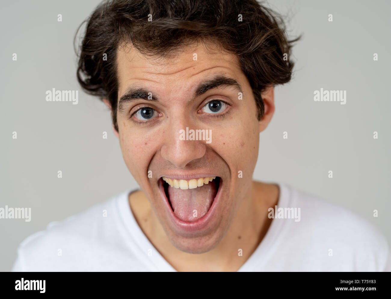 Portrait of young millennial funny male having fun bursting into laughing loudly after hearing humor anecdotes and jokes. Isolated against neutral bac Stock Photo