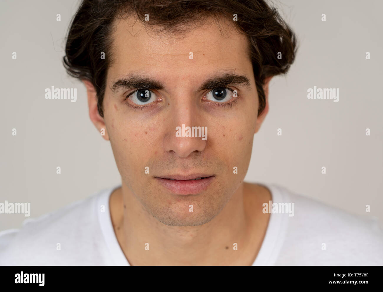 Close up headshot of young latin man with natural and serious face and funny look. Isolated on neutral background. In People, fashion, lifestyle Beaut Stock Photo