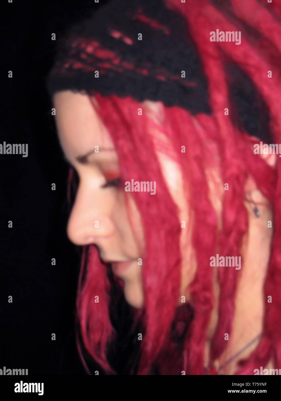 Blurred face portrait closeup of young independent caucasian teenager girl looking down with colourful unusual vibrant red dyed dreadlocks hair Stock Photo