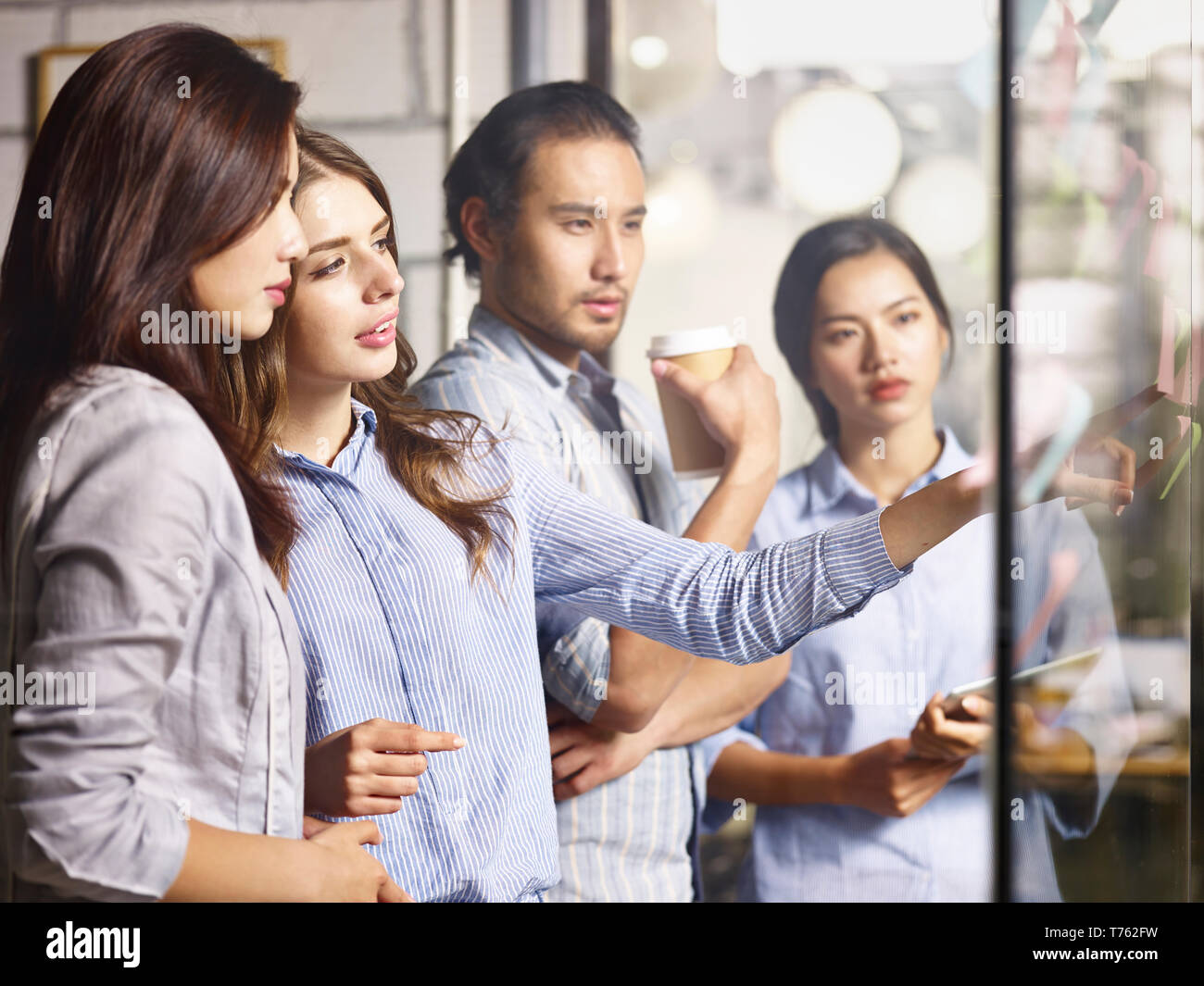 team of young asian and caucasian entrepreneurs discussing business using adhesive notes in office. Stock Photo